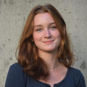 Brigitte Young wearing a blue shirt in front of a concrete wall