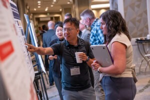 Ori Borjigin in conversation with conference attendee and pointing to presentation poster